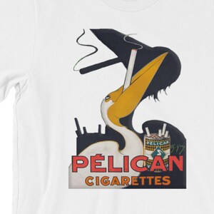 Könnte beinhalten: Ein weißes T-Shirt mit einer Vintage-Werbung für Pelican-Zigaretten. Die Anzeige zeigt einen Zeichentrick-Pelikan, der eine Zigarette raucht, mit dem Text "PÉLICAN CIGARETTES".