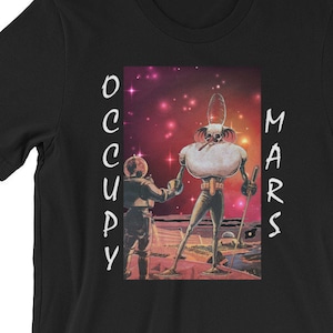 Puede incluir: Camiseta negra con un gráfico de dos figuras de pie en un planeta con un fondo de cielo estrellado. El texto "OCCUPY MARS" está impreso verticalmente en los lados izquierdo y derecho del gráfico.