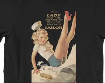 Peut inclure: T-shirt noir avec une illustration vintage d'une femme portant un chapeau de marin et un haut blanc avec un short bleu. Le texte "I'm a Lady with the vocabulary of a well educated Sailor" est imprimé sur le t-shirt.