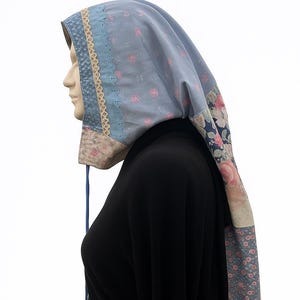 May include: A light blue bonnet with a floral patchwork design. The bonnet features a lace trim and a drawstring closure. The fabric has a pattern of pink roses and small blue flowers.