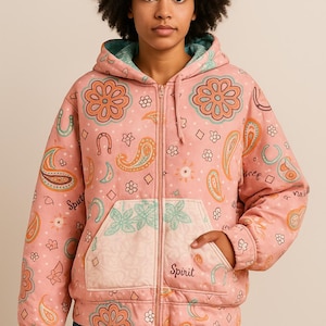 May include: A pink zip-up hoodie with a floral and paisley pattern. The jacket features a hood with a teal lining, a front pocket with the word "Spirit", and a full-length zipper. The design includes flowers, horseshoes, and paisley shapes.