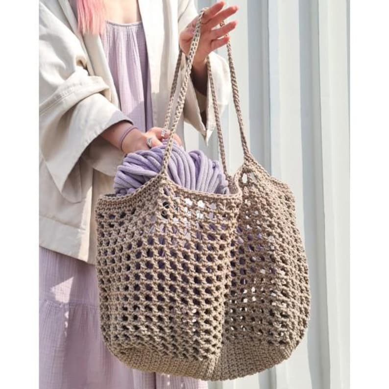 May include: A beige crocheted tote bag with a large mesh pattern. The bag is filled with a bundle of lavender yarn.