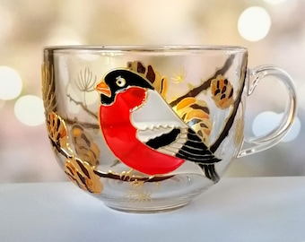 May include: A clear glass mug with a hand-painted design of a red-breasted robin perched on a branch with gold pine cones.