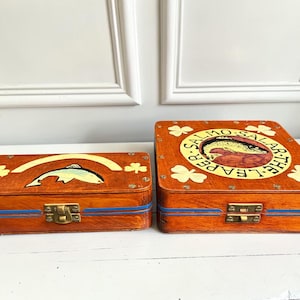 May include: Two rectangular wooden boxes with brass latches and blue painted stripes. The smaller box features a painted fish and shamrocks. The larger square box displays a circular graphic with a fish and the text SALMO SALAR THE LEAPER.