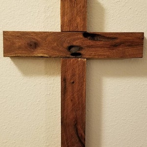 May include: A wooden cross made of four pieces of wood, stained a dark brown color. The cross is mounted on a white wall.