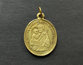 May include: An oval gold-toned metal pendant featuring a relief image of Saint Joseph holding the infant Jesus. The text S. JOSEPH MODEL OF PURITY PRAY FOR US is embossed around the central figures, with a small loop at the top for hanging.