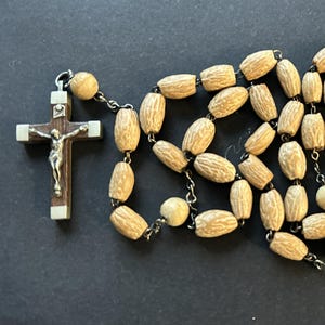 May include: A rosary with light brown, oblong beads and a silver crucifix. The crucifix has a silver figure of Jesus Christ and is set on a dark brown wooden cross with silver accents. The beads are connected by a silver chain.