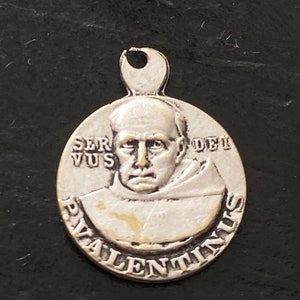 May include: Silver pendant featuring a portrait of Saint Valentine, with the inscription "Servus Dei" and "Valentinus" around the edge.