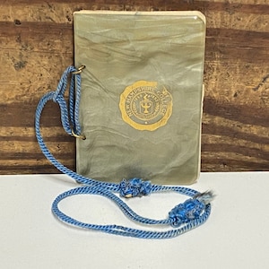 May include: A small, gray, plastic-covered notebook with a gold seal that reads "New Hampshire College 1893" and a blue cord attached.