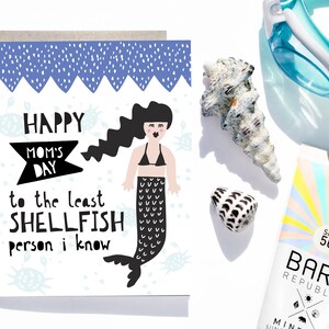 May include: A white card with a blue and white background featuring a mermaid illustration and the text "Happy Mom's Day to the least shellfish person I know".