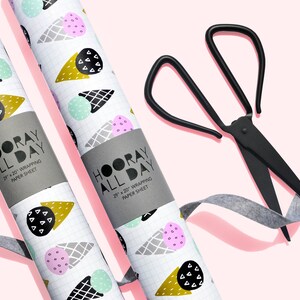 May include: Two rolls of white wrapping paper with a pattern of ice cream cones in pink, blue, and gold. The paper is labeled "HOORAY ALL DAY" and "22" x 20" WRAPPING PAPER SHEET". A pair of black scissors and a gray ribbon are also in the image.