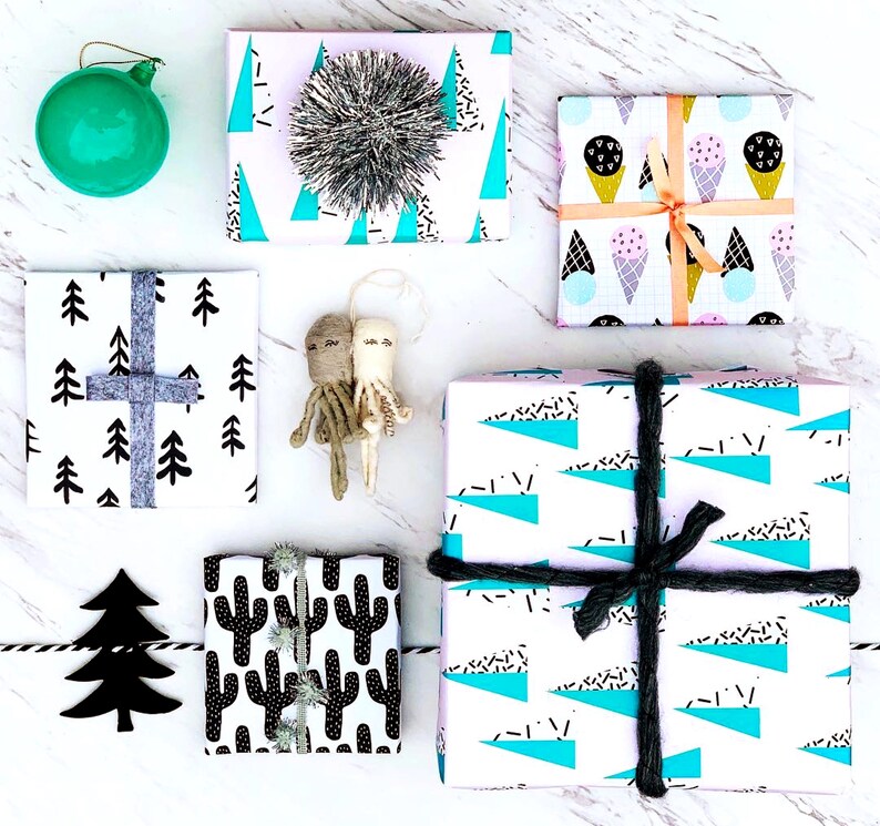 May include: Assortment of gift wrap featuring various patterns, including geometric shapes, trees, and cacti. The wrapping paper is in black, white, blue, pink, and green.