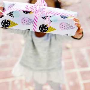 May include: A white gift box with a pink and white striped ribbon. The box is wrapped in paper with a pattern of ice cream cones and polka dots.