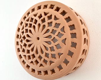 May include: A circular terracotta wall sconce featuring an intricate, laser-cut floral pattern across its dome-shaped surface. The light brown clay fixture has a central circular opening and symmetrical cutouts that create a detailed geometric design.