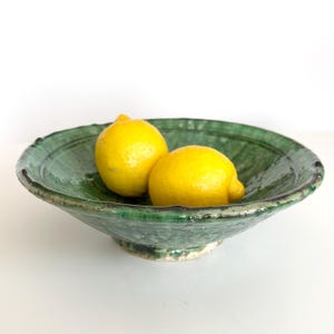 Może przedstawiać: Dwa żółte cytryny w zielonej ceramicznej misce o fakturowanej powierzchni.