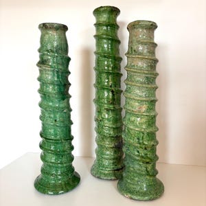 Puede incluir: Tres jarrones altos de cerámica verde con diseño en espiral. Los jarrones tienen una superficie texturizada y un acabado brillante. Los jarrones son de diferentes tonos de verde. Los jarrones se exhiben sobre una superficie blanca. Cada jarrón mide unos 40 cm de alto.