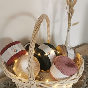 May include: A wicker basket filled with colorful yarn balls, including red, black, beige, and pink. The yarn is labeled "Rainbow" and is arranged in a decorative way. The basket is decorated with string lights.