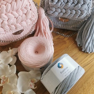 May include: Two crocheted handbags, one pink and one gray, with matching yarn skeins. The yarn is labeled "Rainbow T-shirt Yarn 100% Cotton".