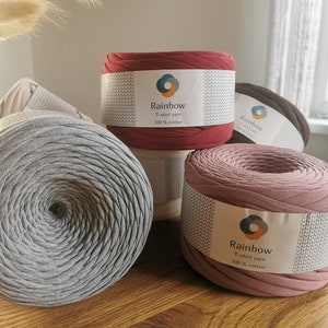 May include: Four spools of t-shirt yarn in different colors: gray, beige, pink, and red. Each spool has a label that says "Rainbow T-shirt yarn 100% cotton".