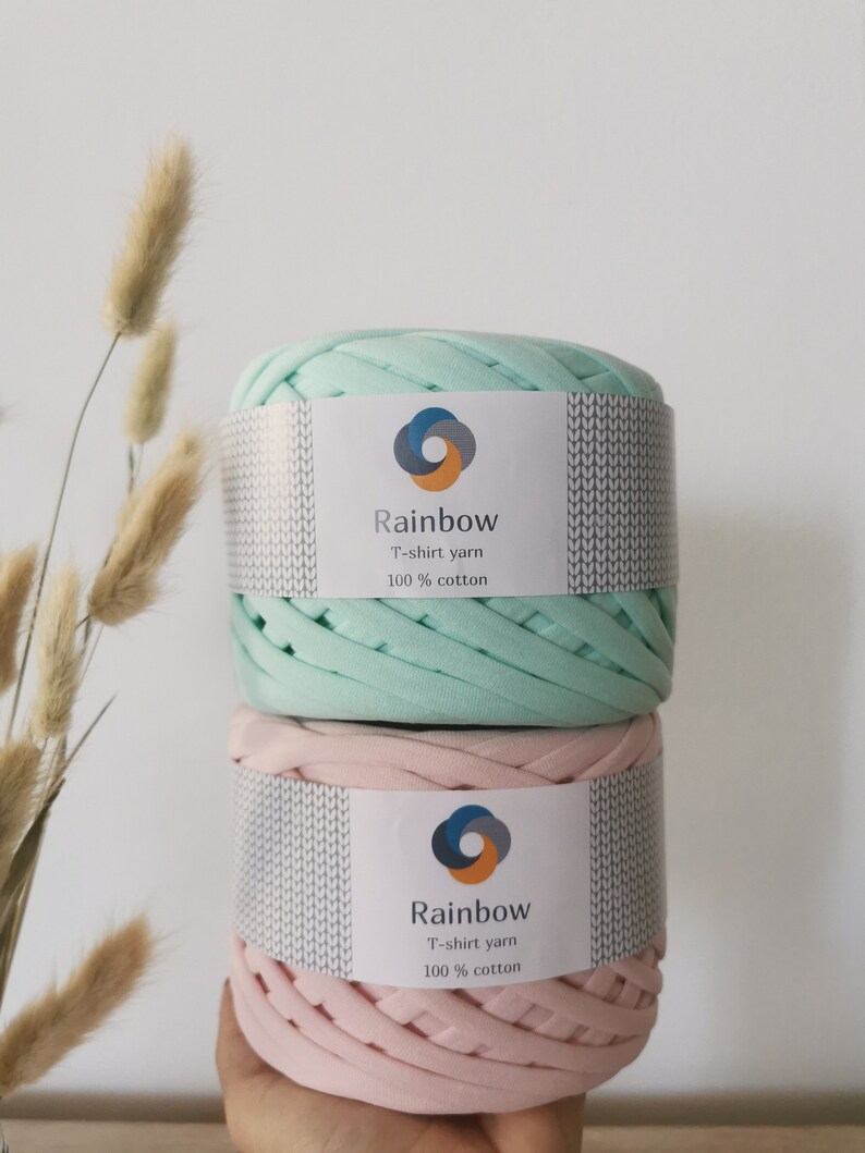 May include: Two spools of t-shirt yarn, one in light green and one in pink. Both spools have a white label with the text "Rainbow T-shirt yarn 100% cotton".