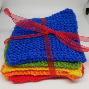 Peut inclure: Un ensemble de débarbouillettes tricotées à la main aux couleurs de l'arc-en-ciel : rouge, orange, jaune, vert et bleu. Les débarbouillettes sont liées par un ruban rouge transparent, créant un ensemble soigné. La texture tricotée est visible.