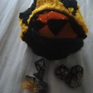 May include: A black and yellow crocheted pouch with a zipper opening, containing a set of black and gold dice. The dice are numbered 1-6, 8, 10, 12, 16, 17, 30, 50.
