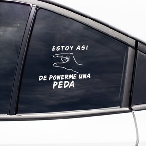 May include: A white car window with a white vinyl decal. The decal features a hand gesture and text in Spanish that reads "ESTOY ASI DE PONERME UNA PEDA."