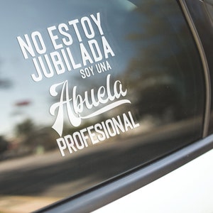 May include: A white vinyl sticker on a car window with the text "No estoy jubilada soy una Abuela profesional" in Spanish.