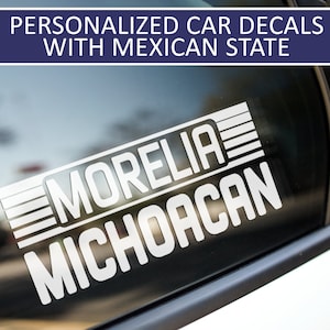 May include: White vinyl car decal with the text "Morelia Michoacan" in a bold, blocky font. The decal is on a black car window.