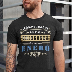 May include: A black t-shirt with a vintage-style graphic that reads "*¡COMPROBADO! *
★ Los Mas ✶✶
CHINGONES
Nacen en
ENER()"
