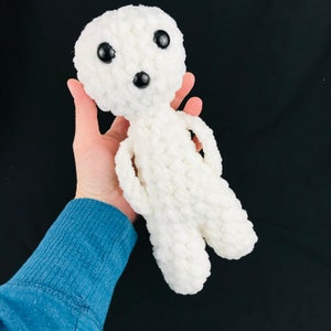 May include: A white crocheted plush toy with black eyes and a black nose. The toy is shaped like a person and has a simple design.