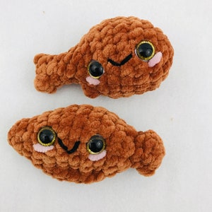 Könnte beinhalten: Zwei braune gehäkelte Plüschtiere in Form von Hähnchenschenkeln mit Glitz Augen und lächelnden Gesichtern.