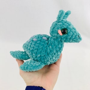 May include: A teal blue crocheted plush toy shaped like a seahorse with large black eyes and pink cheeks.