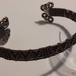 Peut inclure: Un bracelet en fil de cuivre avec un motif tissé et une spirale décorative à chaque extrémité.