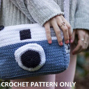Op de afbeelding: Een gehaakte cameratas in blauw, wit en zwart. De tas heeft een band en een knoopsluiting. CROCHET PATTERN ONLY staat onder de tas.