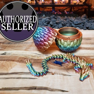 May include: A rainbow iridescent dragon egg shaped trinket box with a matching dragon tail. The box is open and the inside is empty. The dragon tail is curled up on a wooden surface.