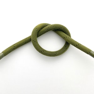 May include: A green cord tied in a knot. The cord is made of a woven material and has a slightly textured surface.