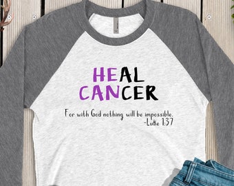 May include: A white and grey raglan shirt with the words "HEAL CANCER" in purple and black, and the Bible verse Luke 1:37. The shirt is styled with blue jeans and white Converse trainers.