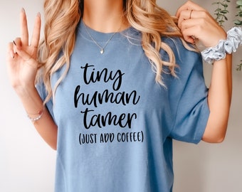 May include: A light blue t-shirt with the text "tiny human tamer (JUST ADD COFFEE)" printed in black.