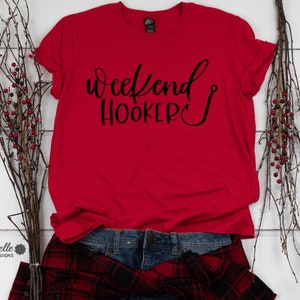 Peut inclure: T-shirt rouge avec le texte "Weekend Hooker" en lettres cursives noires avec un hame&ccedil;on &agrave; la fin du mot "Hooker".