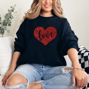 Puede incluir: Una sudadera negra con un coraz&oacute;n rojo de purpurina que dice "love".