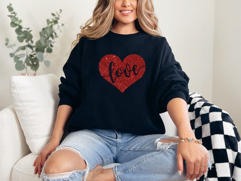 Puede incluir: Una sudadera negra con un coraz&oacute;n rojo de purpurina que dice "love".