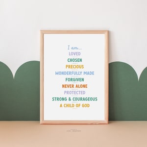 May include: A framed print with a light wood frame and a white background. The print features a list of positive affirmations in colorful text, including "I am... Loved, Chosen, Precious, Wonderfully Made, Forgiven, Never Alone, Protected, Strong & Courageous, A Child of God".