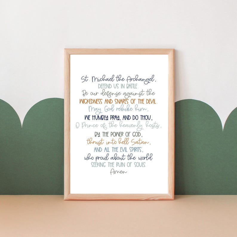 May include: A printable wall art print with a light brown wood frame. The print features a white background with a blue and orange text that reads "St. Michael the Archangel. Defend us in battle. Be our defense against the wickedness and snares of the devil. May God rebuke him. We humbly pray, and do thou, O Prince of the heavenly hosts. By the power of God, thrust into hell Satan, and all the evil spirits, who prowl about the world seeking the ruin of souls. Amen."