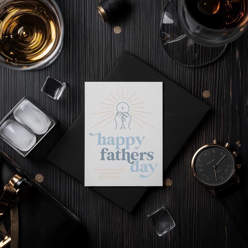 A white greeting card with "happy fathers day" and a communion host graphic is on a black envelope, surrounded by ice cubes, drinks, and a watch on a dark wood table.