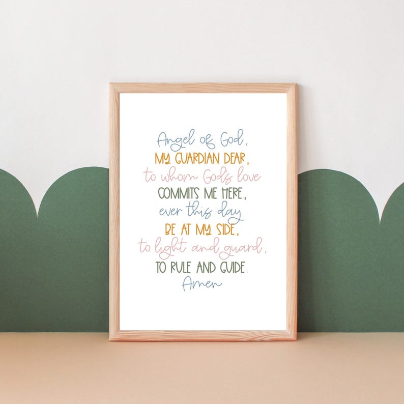 May include: A framed print with a light brown frame and a white background. The print features a handwritten prayer in blue, pink, and yellow text that reads "Angel of God, My Guardian Dear, to whom God's love commits me here, ever this day be at my side, to light and guard, to rule and guide. Amen."