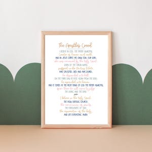 May include: A framed print of the Apostle's Creed in a white frame with a light wood border. The text is in blue and pink lettering on a white background. The text includes the words "I believe in God, the Father Almighty, Creator of heaven and earth..."