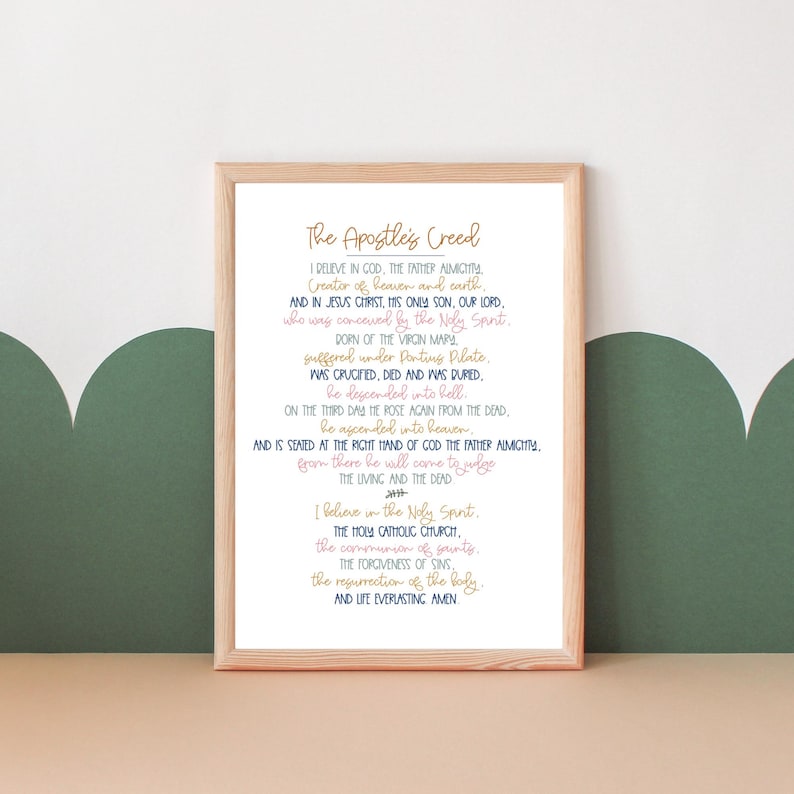 May include: A framed print of the Apostle's Creed in a white frame with a light wood border. The text is in blue and pink lettering on a white background. The text includes the words "I believe in God, the Father Almighty, Creator of heaven and earth..."