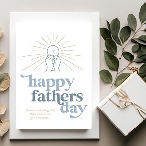 A white greeting card with "happy fathers day" and a communion host graphic is centered on a light gray background, with a white gift box and green leaves.