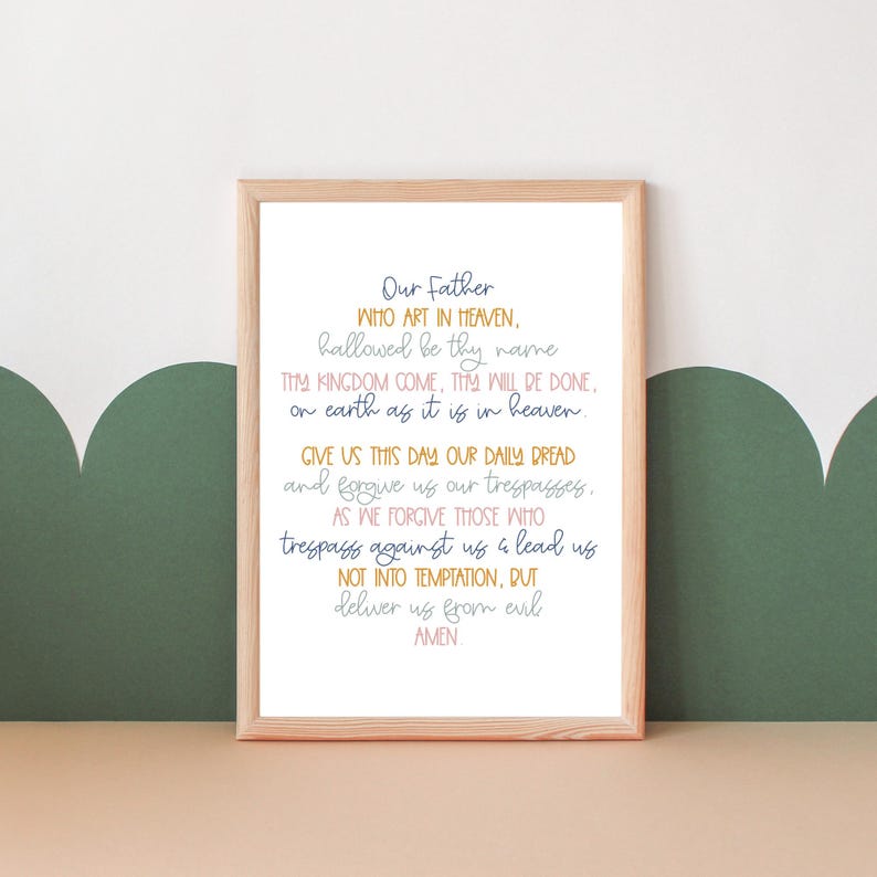 May include: A framed print with a white background and a light brown frame. The print features the Lord's Prayer in a handwritten style with blue, pink, and yellow text.